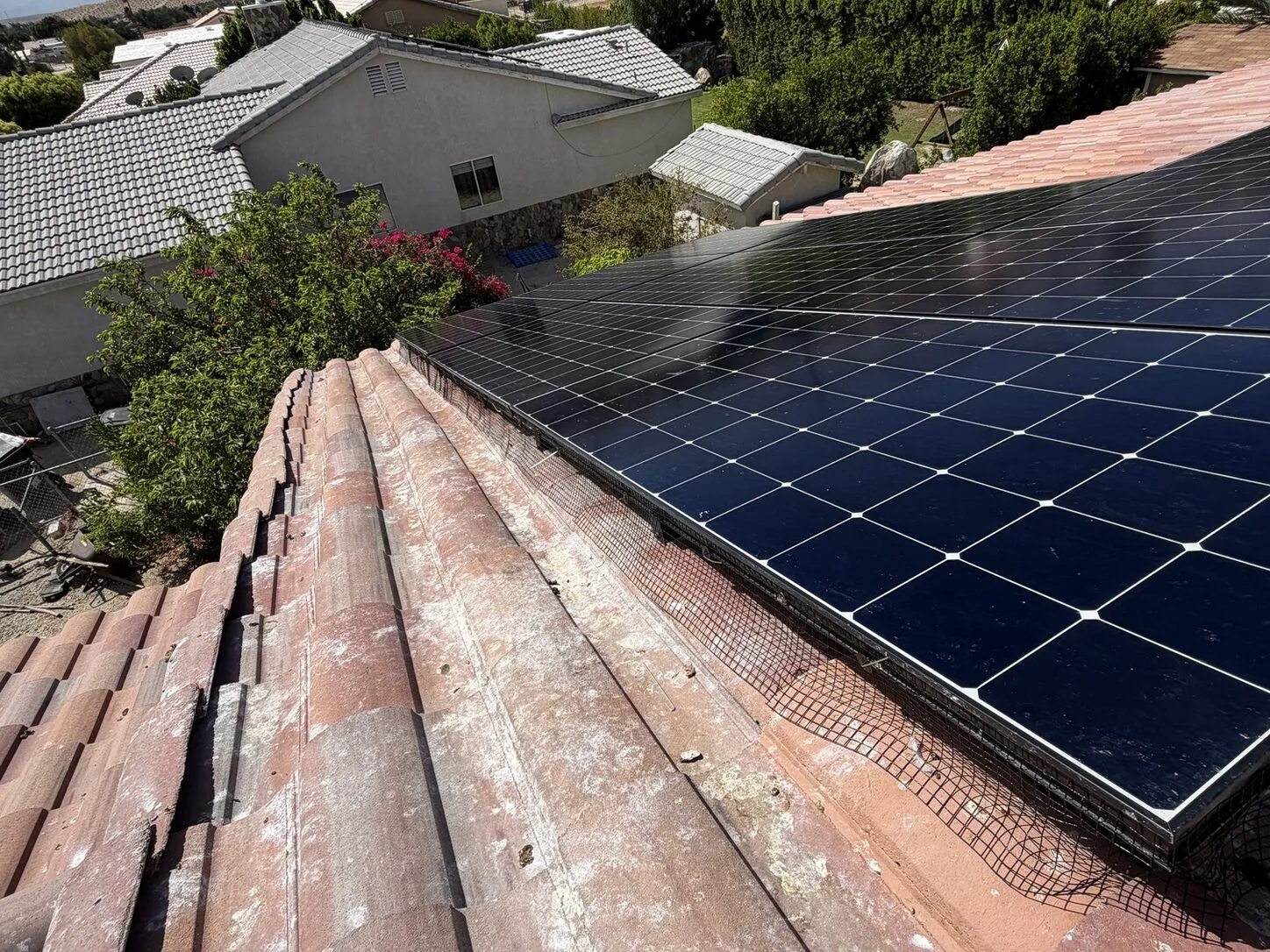 Job photo: critter mesh along the edge of a solar array on a clay-tile roof, with mountains behind
