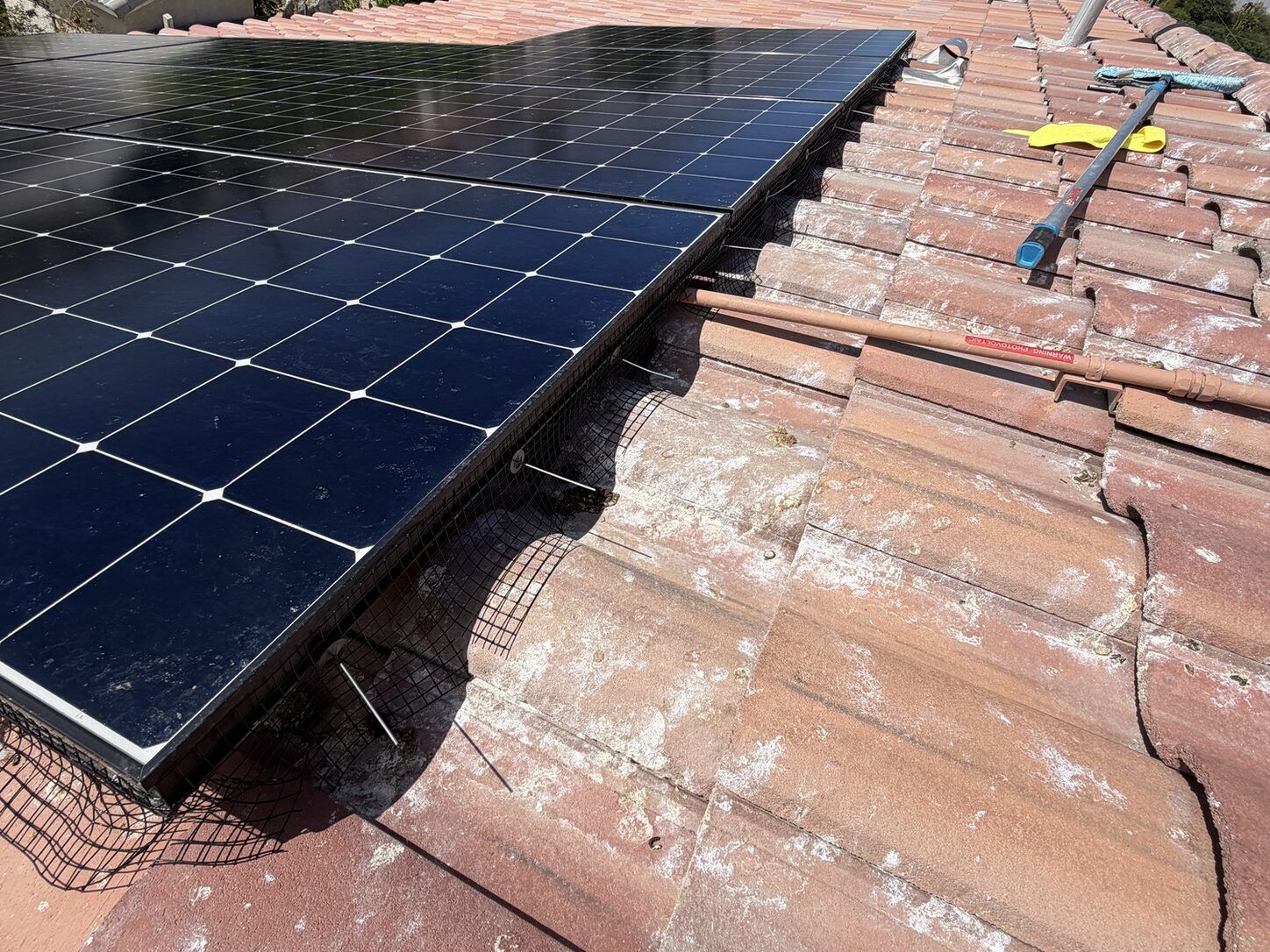 Job photo: critter mesh fitted around the edge of a solar array on a clay-tile roof below the mountains