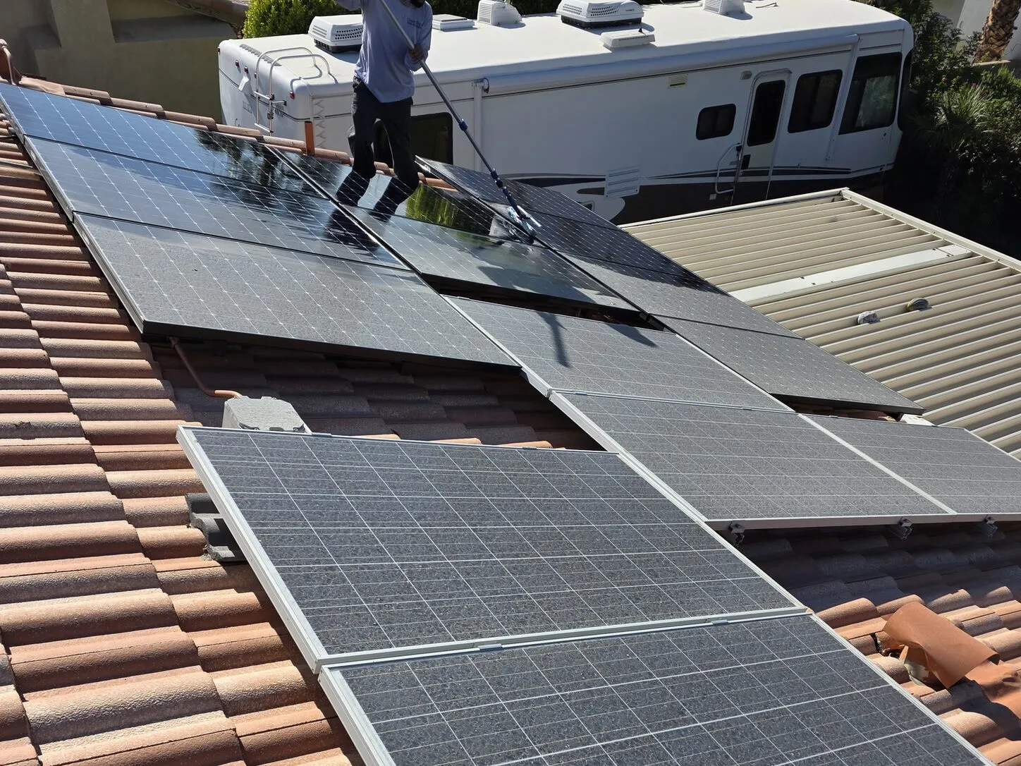 Job photo: a Clear Flow technician working a soft brush across a dusty array on a Cathedral City tile roof