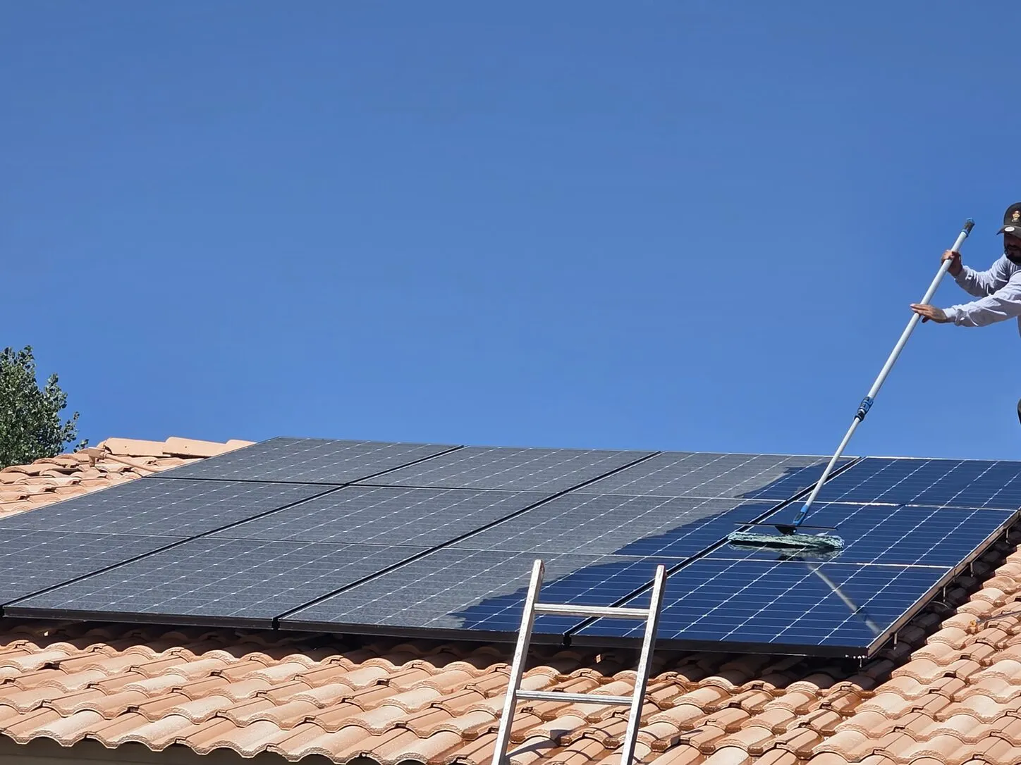 Job photo: a Clear Flow technician running a water-fed brush over solar panels in Palm Desert, with a ladder at the eave