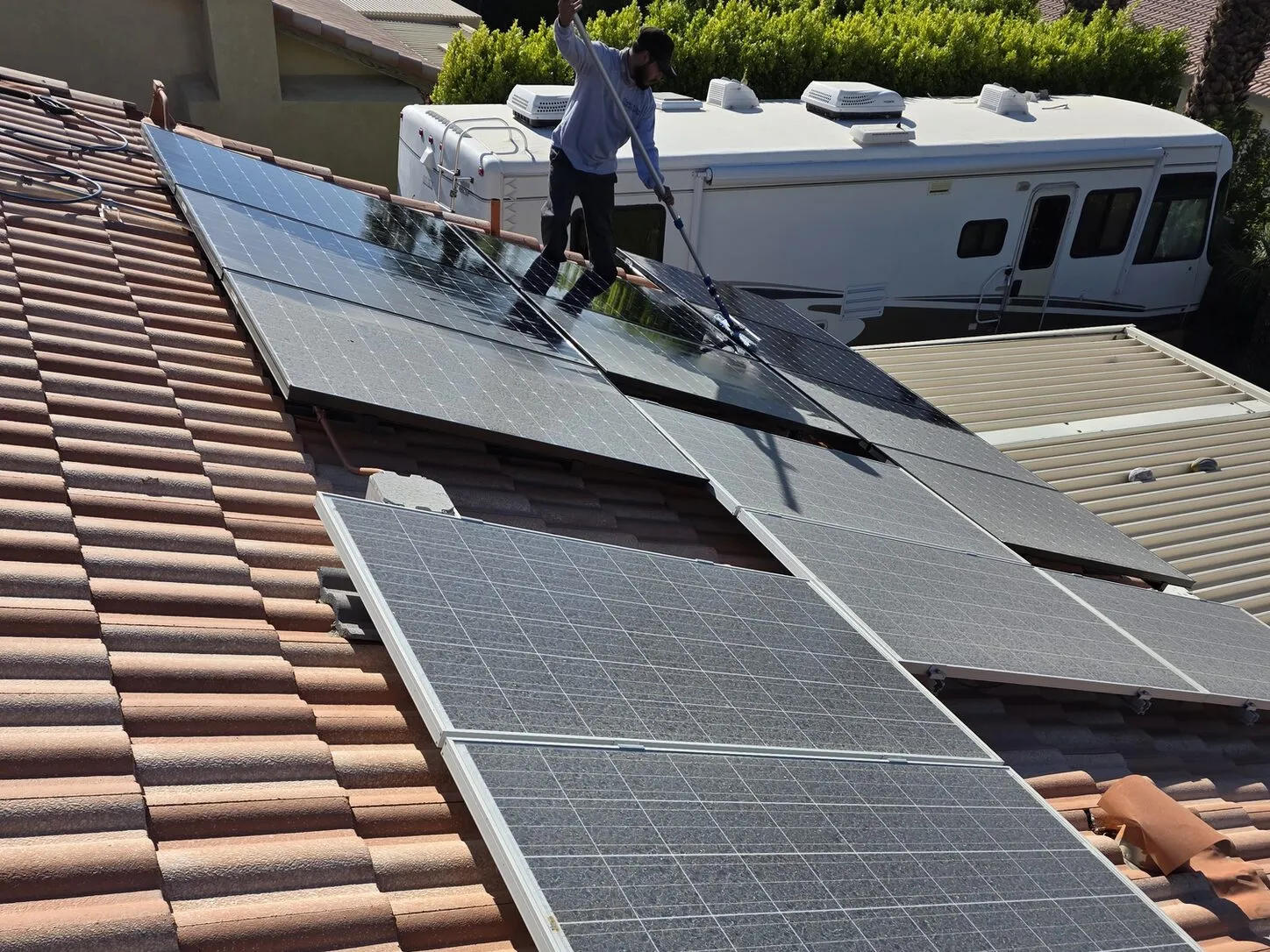 Job photo: a Clear Flow technician brushing a dusty solar array on a Cathedral City clay-tile roof